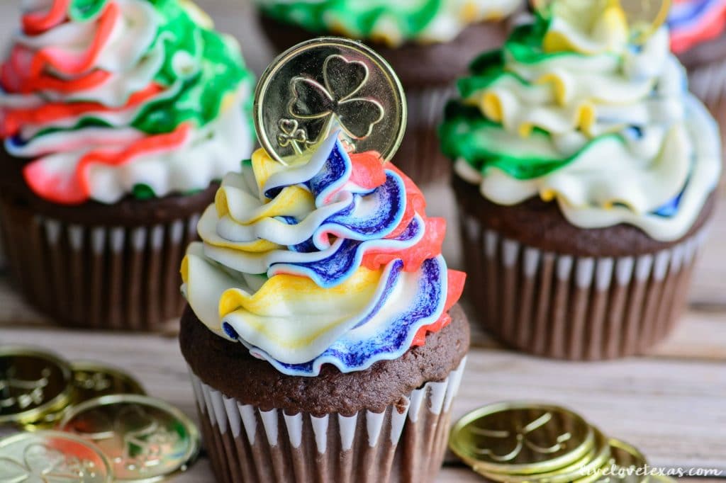 Chocolate cupcakes with rainbow frosting topped with a toy gold coin.