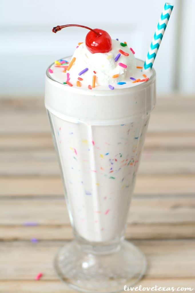 sprinkle milkshake in glass topped with whipped cream and a cherry.
