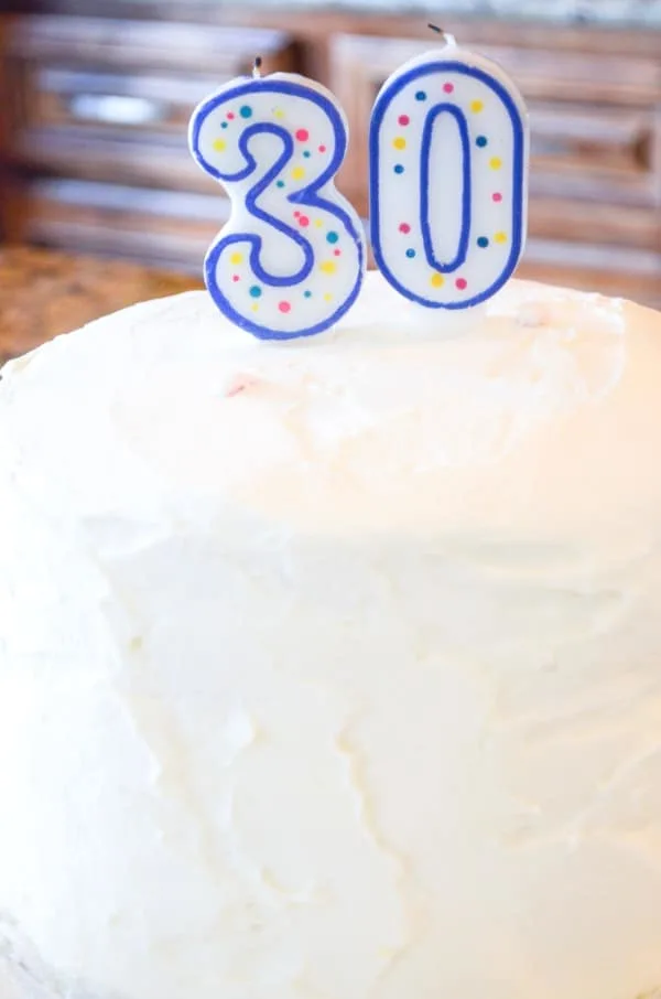 White buttercream frosted rainbow layer cake for 30th birthday party with candles.