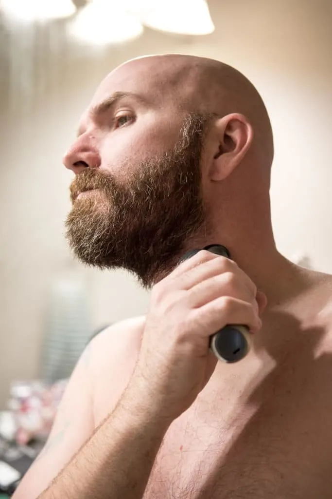 Bald man shaving beard with Norelco beard trimmer.