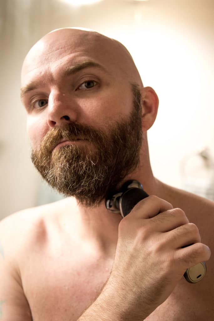 Bald man shaving beard with Philips Norelco beard trimmer.