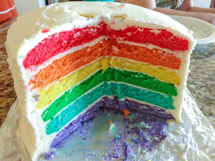 Big rainbow cake with slice cut.