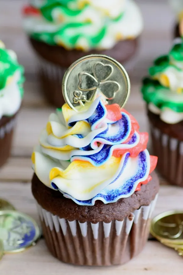 Chocolate cupcakes with rainbow buttercream frosting and topped with a gold coin.