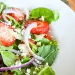 Strawberry salad with feta cheese, pecans, and red onions in white bowl.
