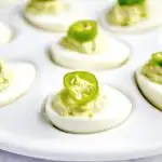 Avocado deviled eggs on platter with jalapeno pepper garnish.