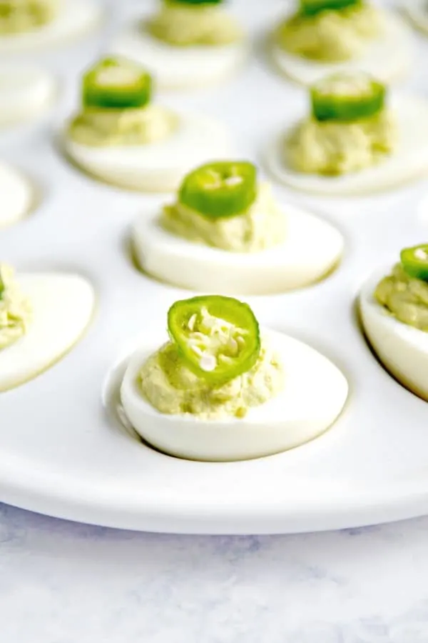 Avocado deviled eggs on platter with jalapeno pepper garnish.