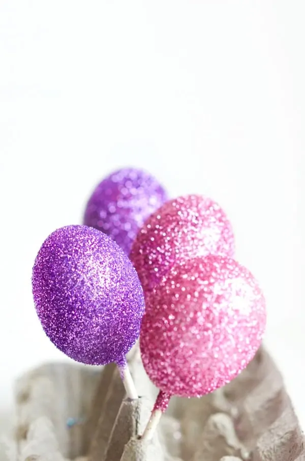 decorated glitter eggs drying on sticks in egg carton