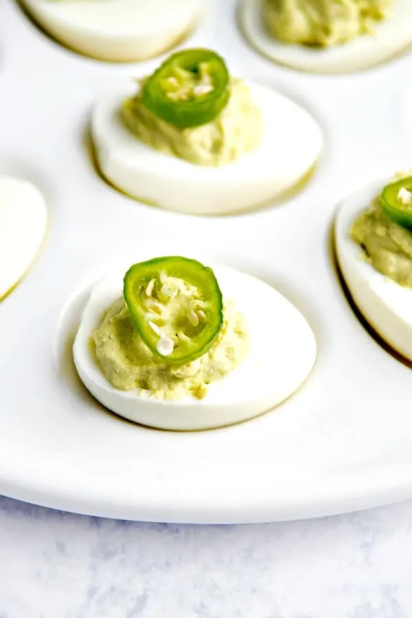Guacamole deviled eggs on white platter.