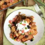 Plate of Cheesy Taco Tater Tot Casserole recipe with casserole pan in background.
