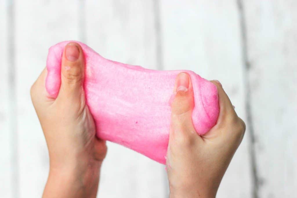 Woman stretching pink sand slime between hands.