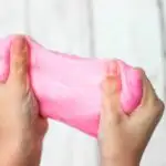 Woman stretching pink sand slime between hands.