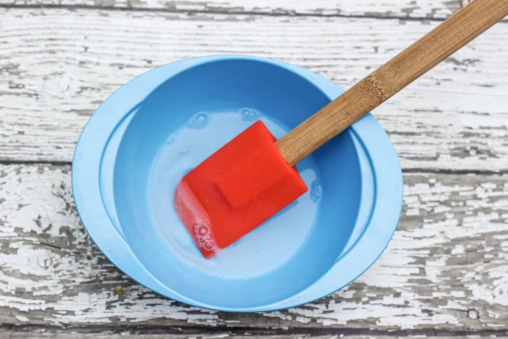 Stretchy sand slime ingredients in mixing bowl with rubber spatula.