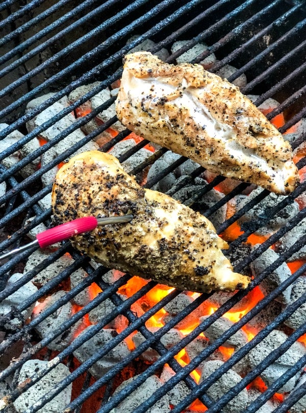 Grilled chicken on charcoal grill with digital thermometer to gauge temperature.