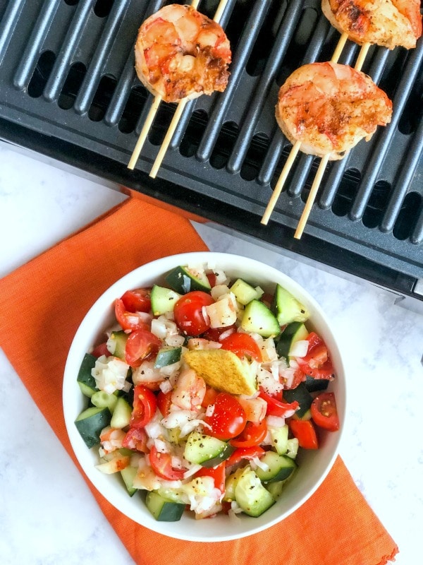 Shrimp on grill with avocado shrimp salad in bowl.
