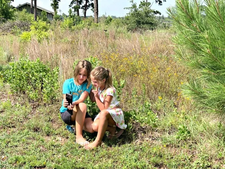 Girls in field taking selfies with cell phone while exploring nature.