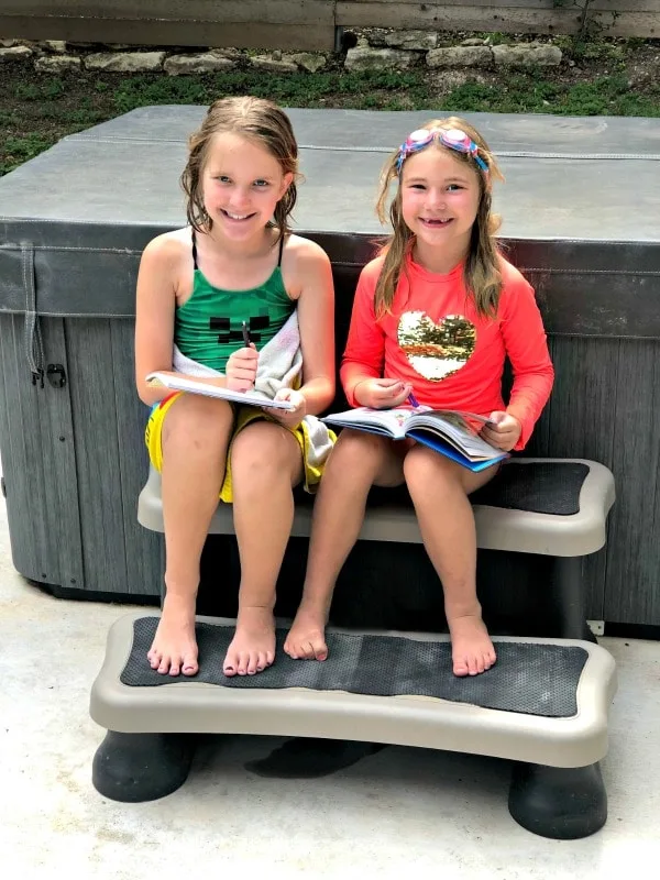Girls reading and writing outside during summer in swimsuits to avoid summer slide.