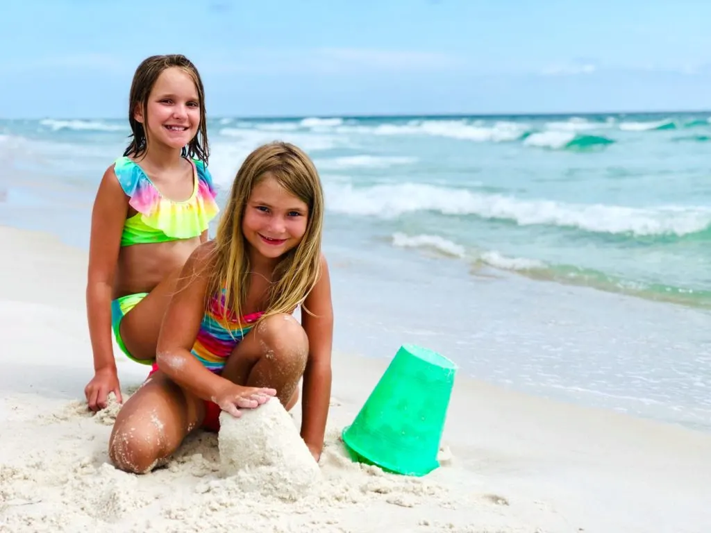 Two sisters playing in the sand on the beach.