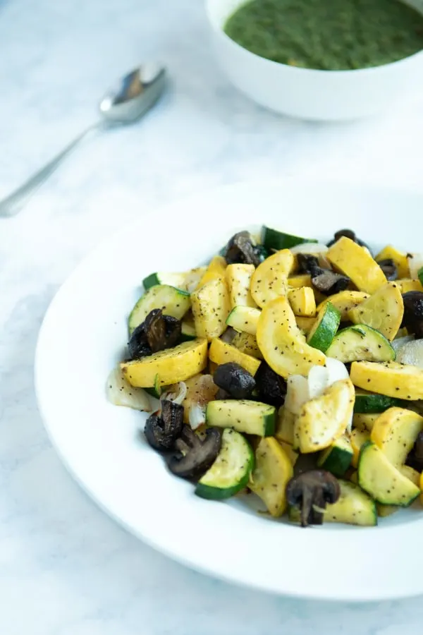 Closeup of oven roasted vegetables with homemade chimichurri sauce in background