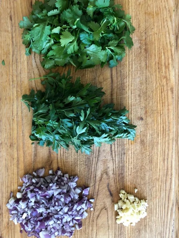 cilantro parsley onion garlic on cutting board for chimichurri sauce