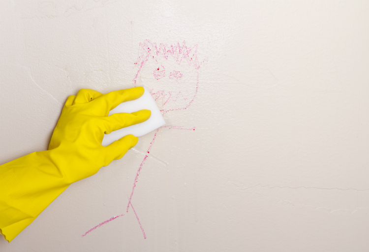 Yellow gloved hand cleaning crayon off wall with magic eraser