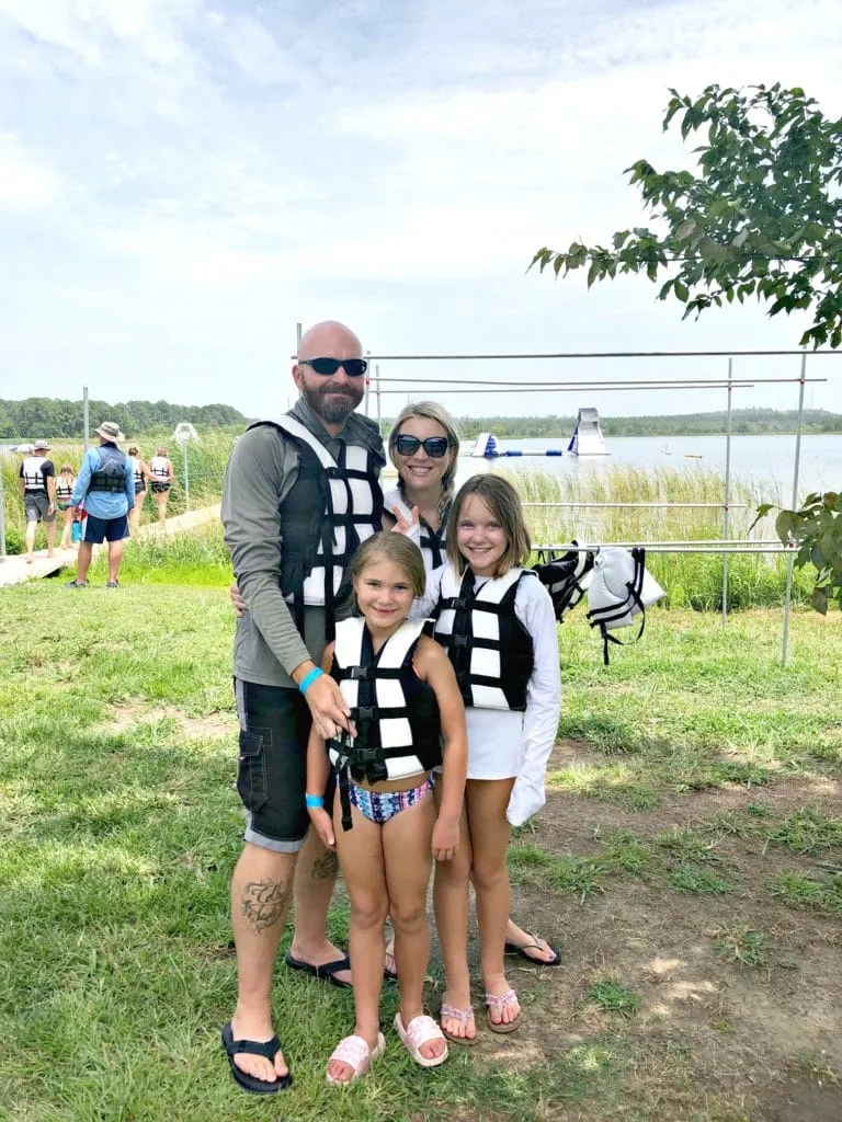 Happy family of four with parents and two girls in life vest at Lake Bastrop in Bastrop Texas outside of Austin.