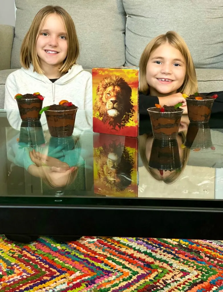 Sisters sitting on colorful rug with Lion King movie and inspired dirt cup dessert recipe.