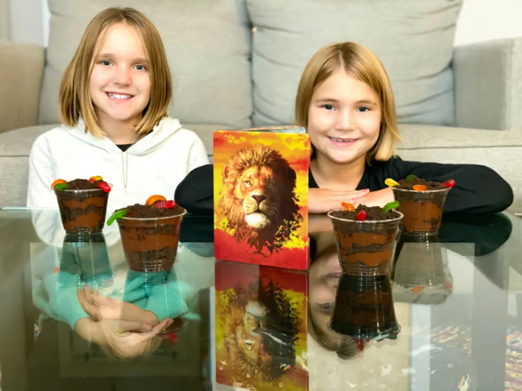 Girls watching The Lion King with dirt cup pudding on table in front of them.