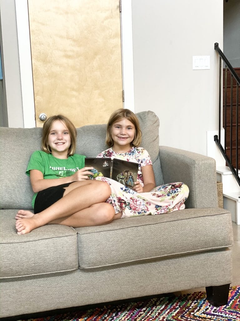 Sisters sitting on loveseat together holding Toy Story 4 DVD