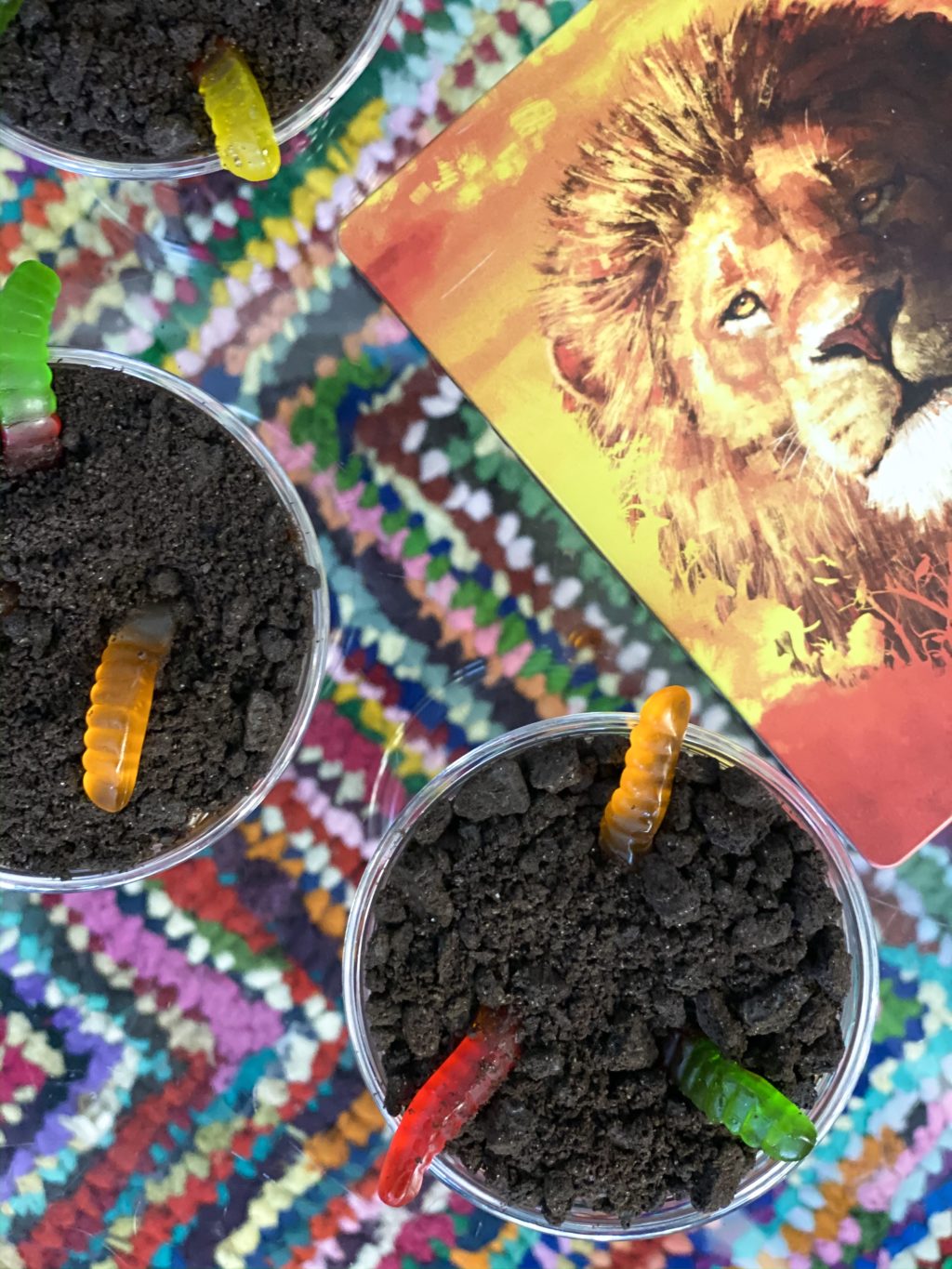Oreo dirt pudding cups with gummy worms on table with colorful rug inspired by The Lion King movie.
