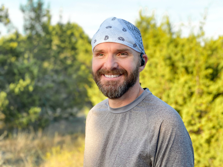 Man smiling before running in front of trees with wireless earbuds in his ears.