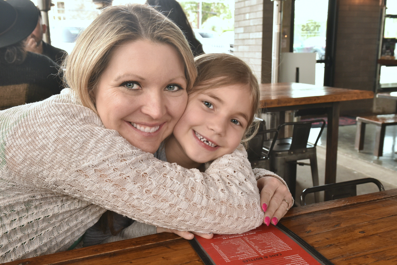 Mom squeezing daughter's neck at restaurant.