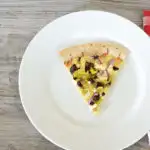 Homemade pizza with artichokes, onions, pepperoccinis, and feta cheese on white plate.