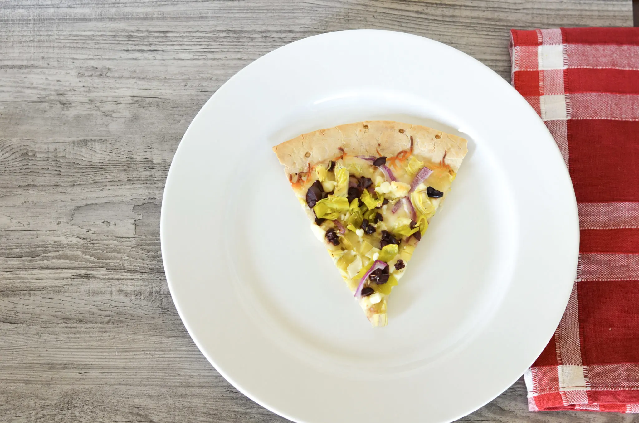 Homemade pizza with artichokes, onions, pepperoccinis, and feta cheese on white plate.
