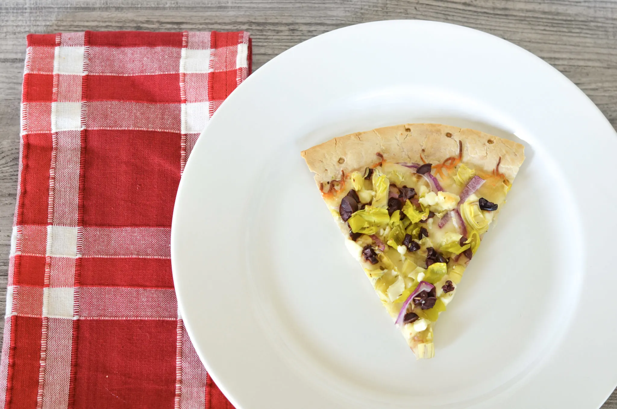 Greek chicken pizza on white plate with checkered napkin on wood table