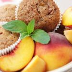 Spiced peach muffins in bowl with fresh peaches