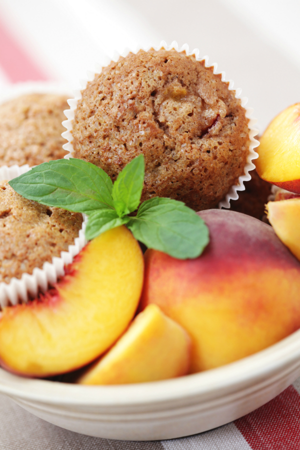 Spiced peach muffins in bowl with fresh peaches