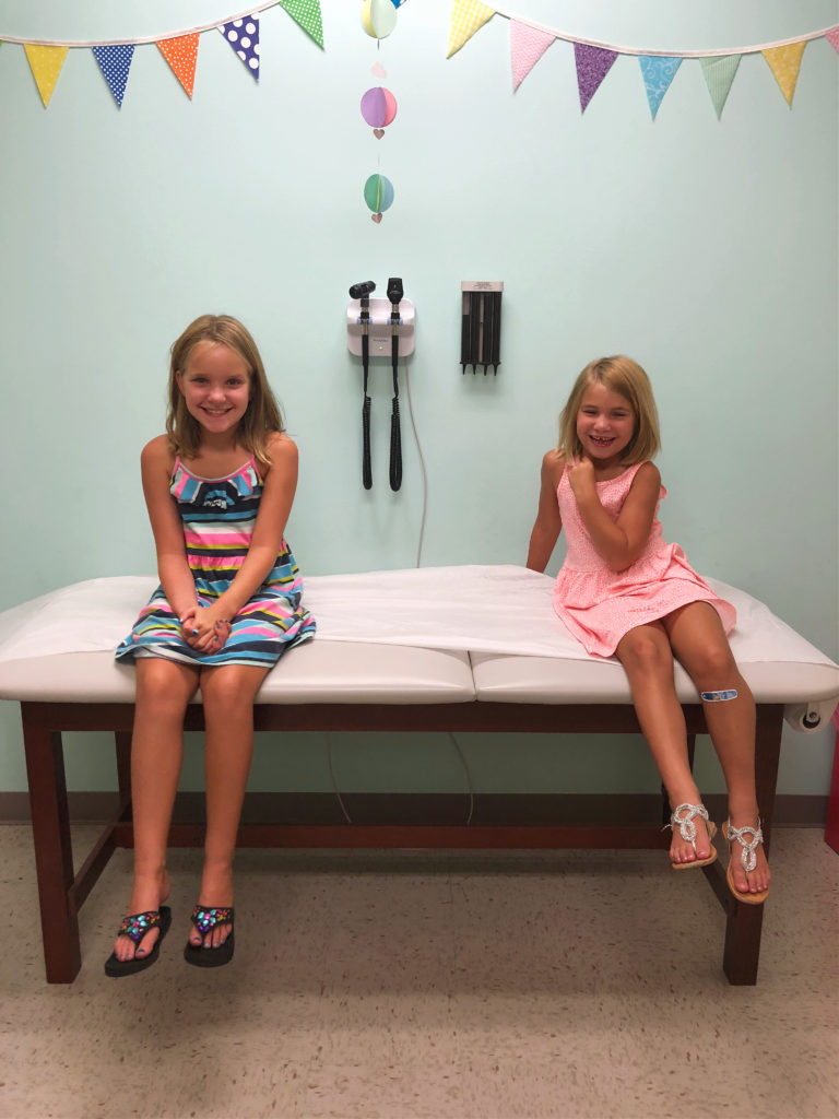 Two young girls sitting on table in pediatrician's office.